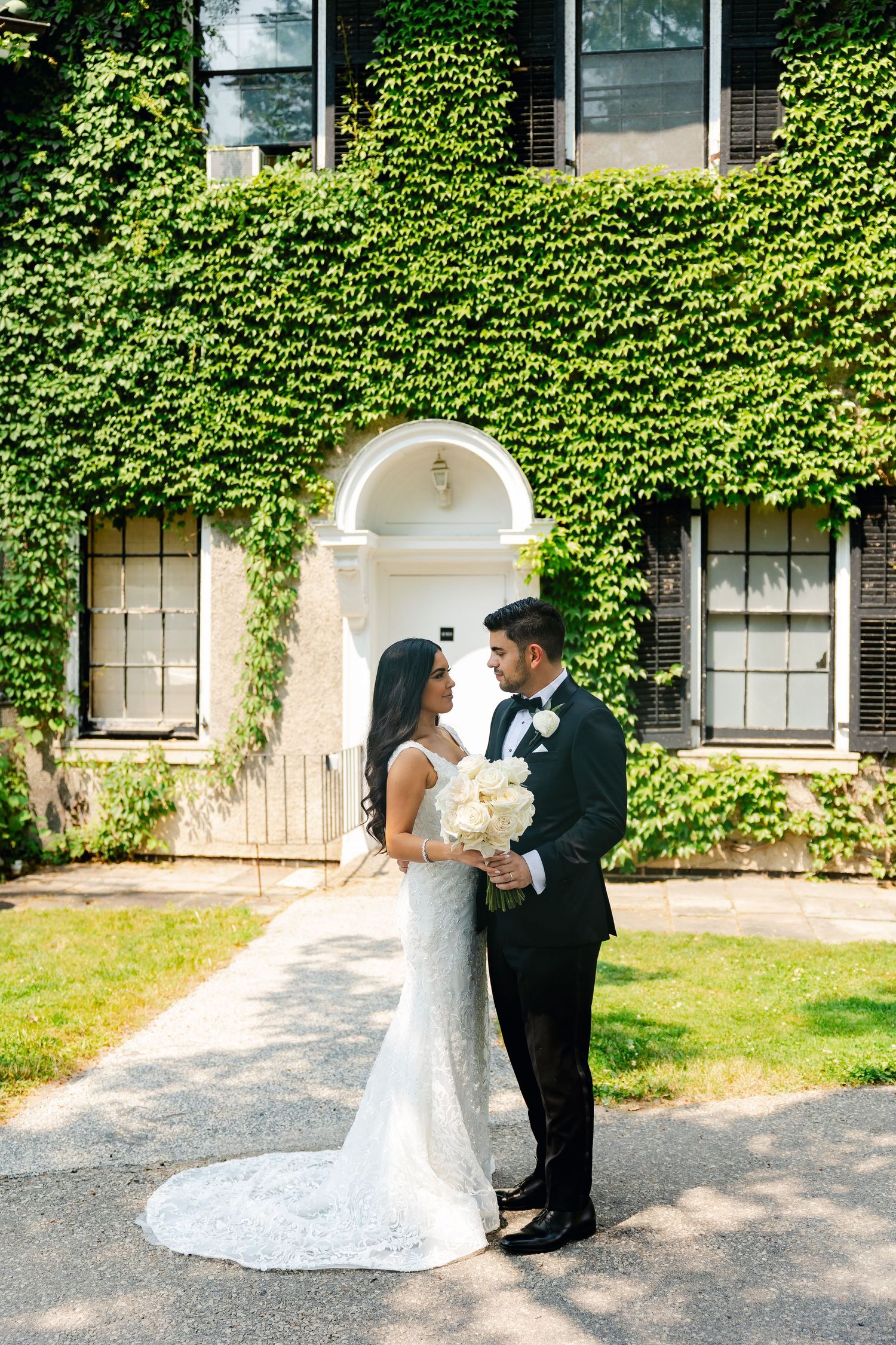 Elegant wedding portrait in front of ivy-covered building featuring white arched entrance.