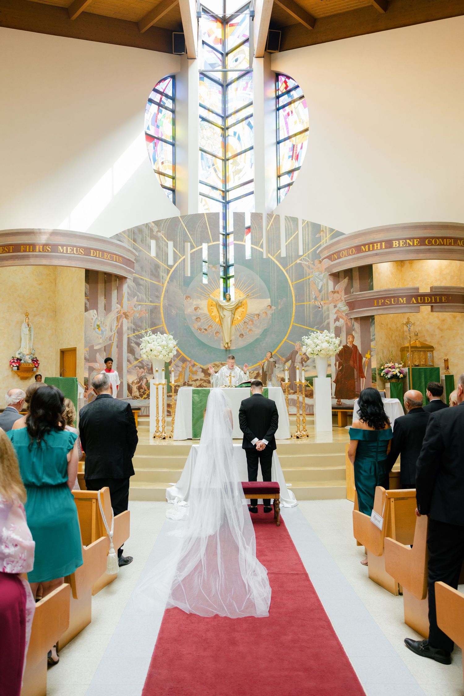 A church wedding ceremony under a beautiful stained glass window and ornate altar.