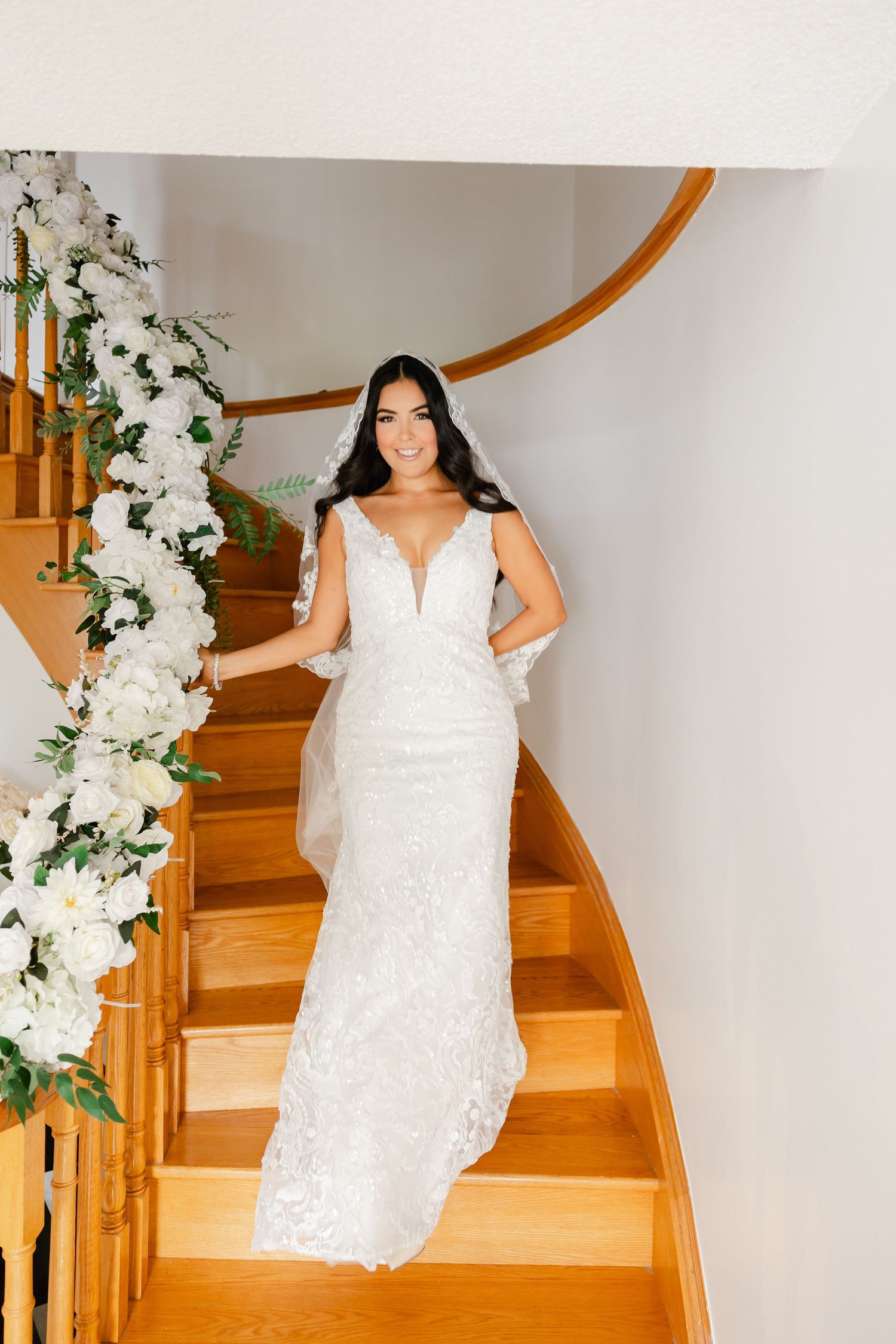 Bride poses on curved wooden staircase decorated with white floral garland.