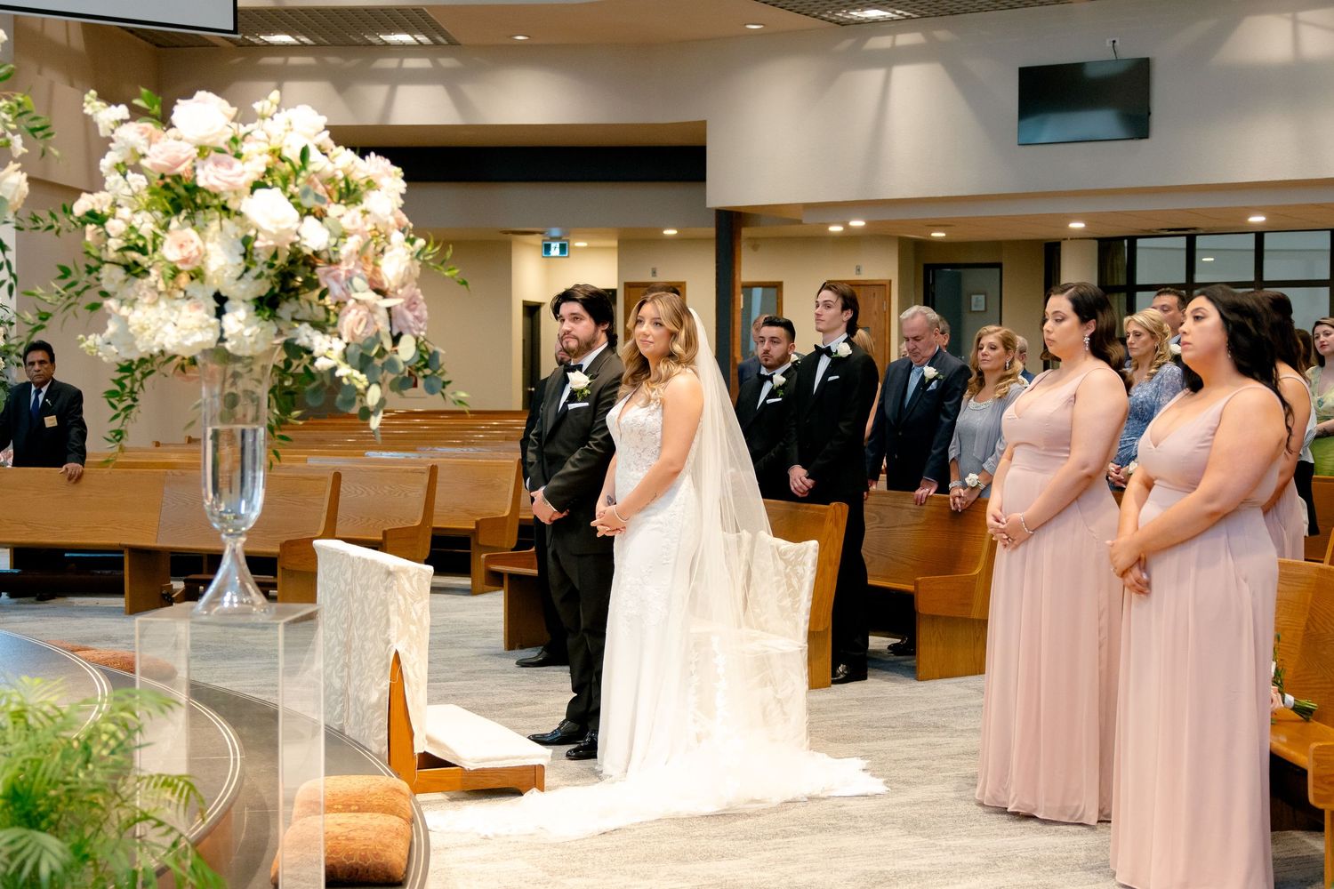 Church wedding ceremony with pink bridesmaid dresses and elegant white floral arrangements.