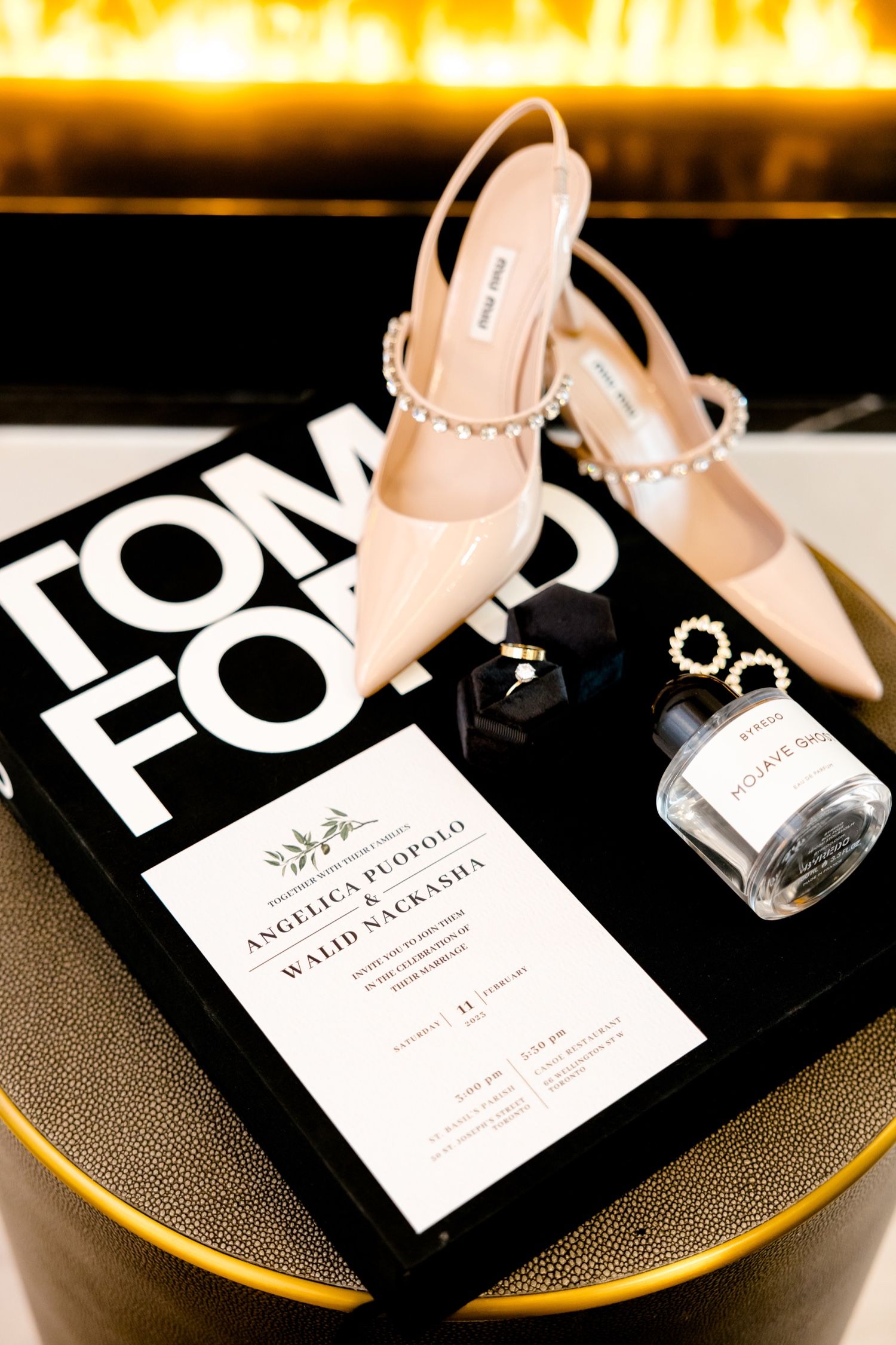 Wedding details including nude heels, invitation and Tom Ford book on a gold-rimmed surface.