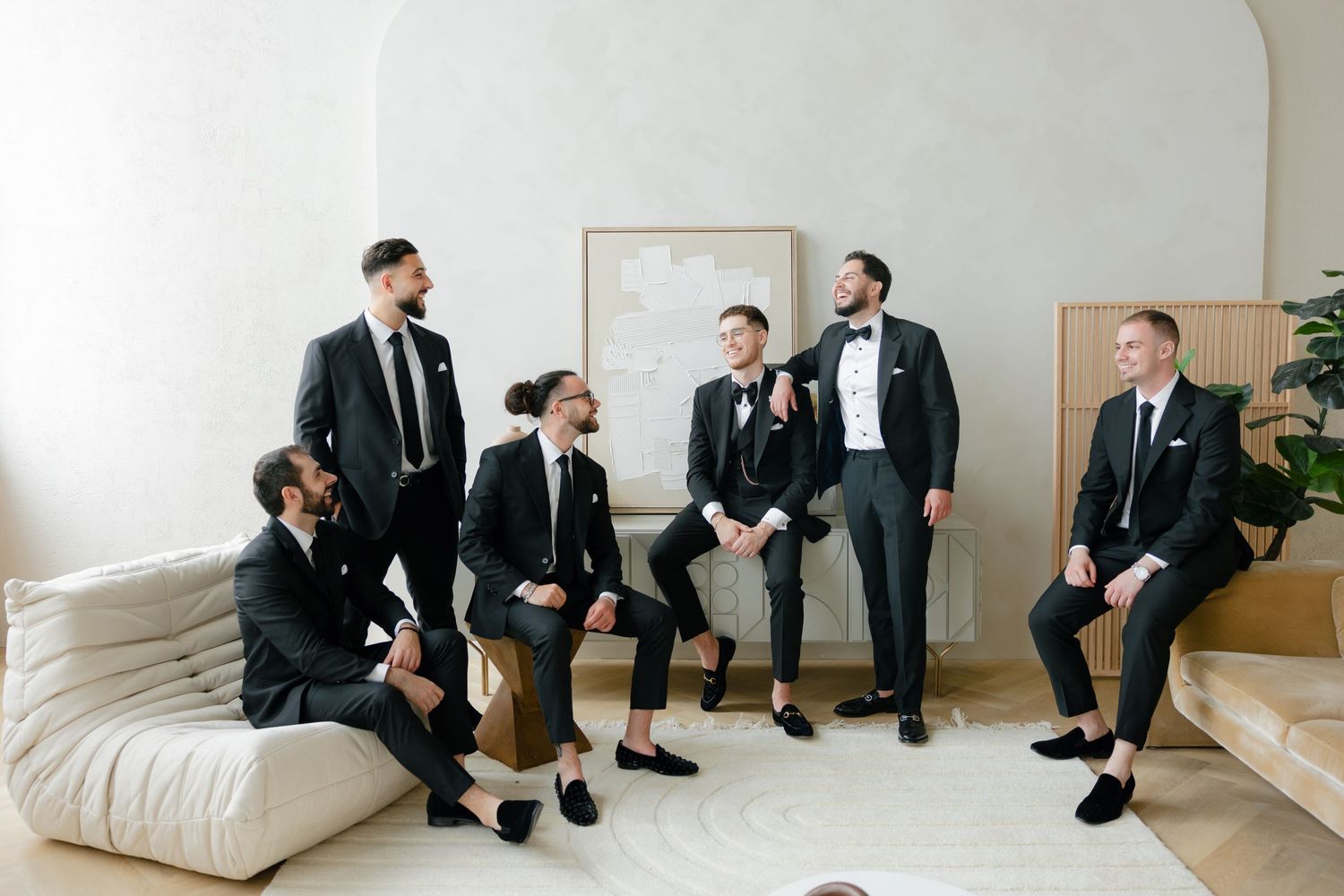 Wedding party members in dark suits gathered casually in minimalist room.