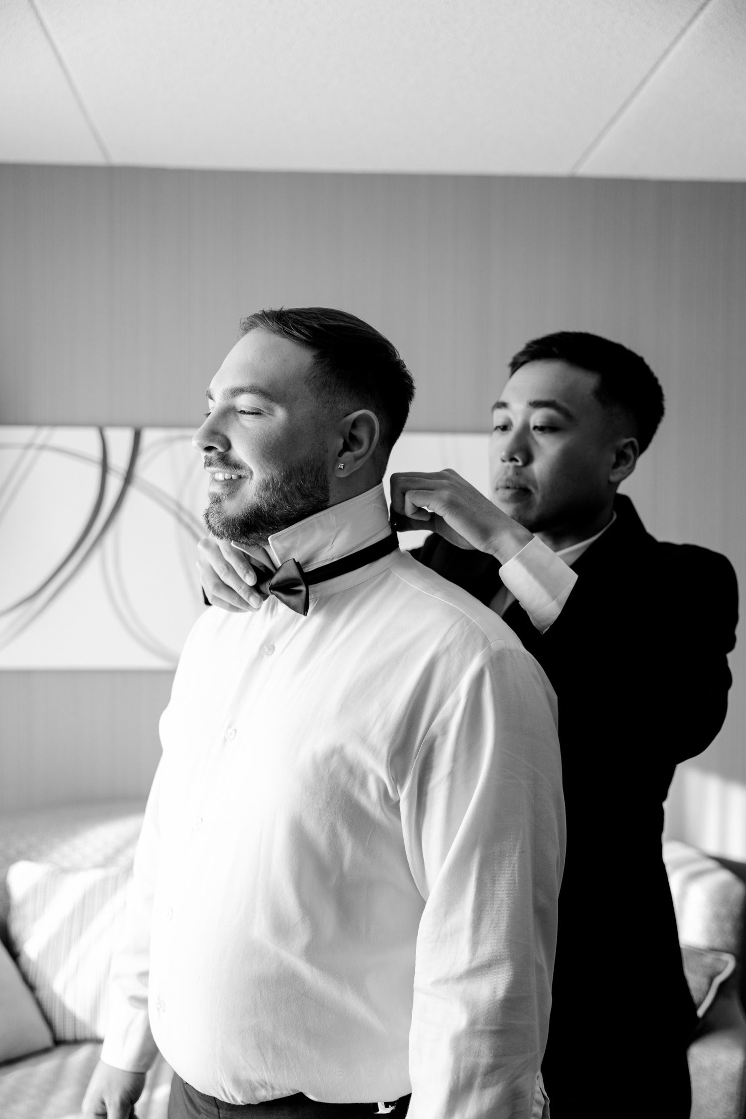 Getting ready moment as groomsman helps adjust bow tie before wedding ceremony.