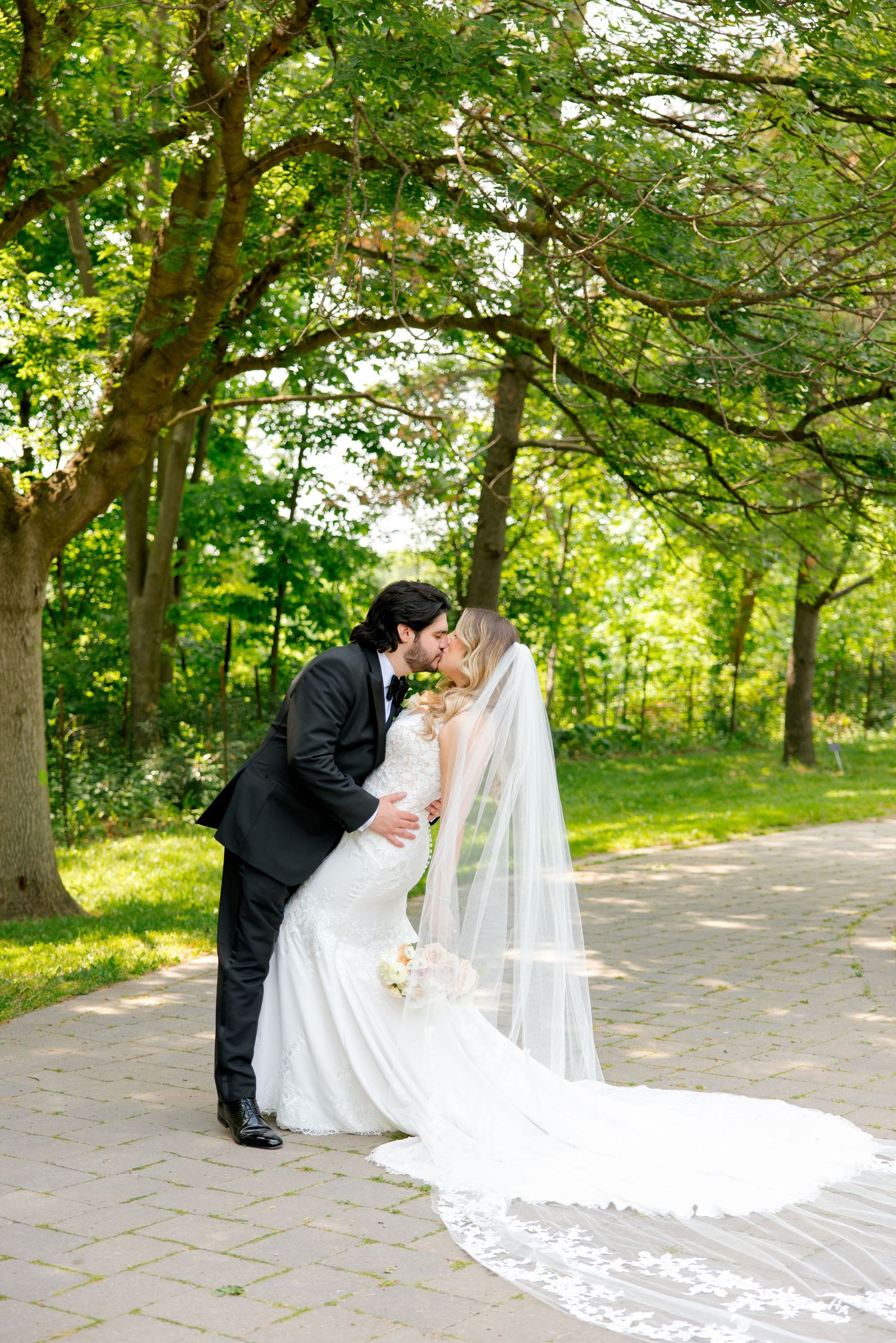 A romantic wedding dip pose captured on a garden path with flowing white veil details.