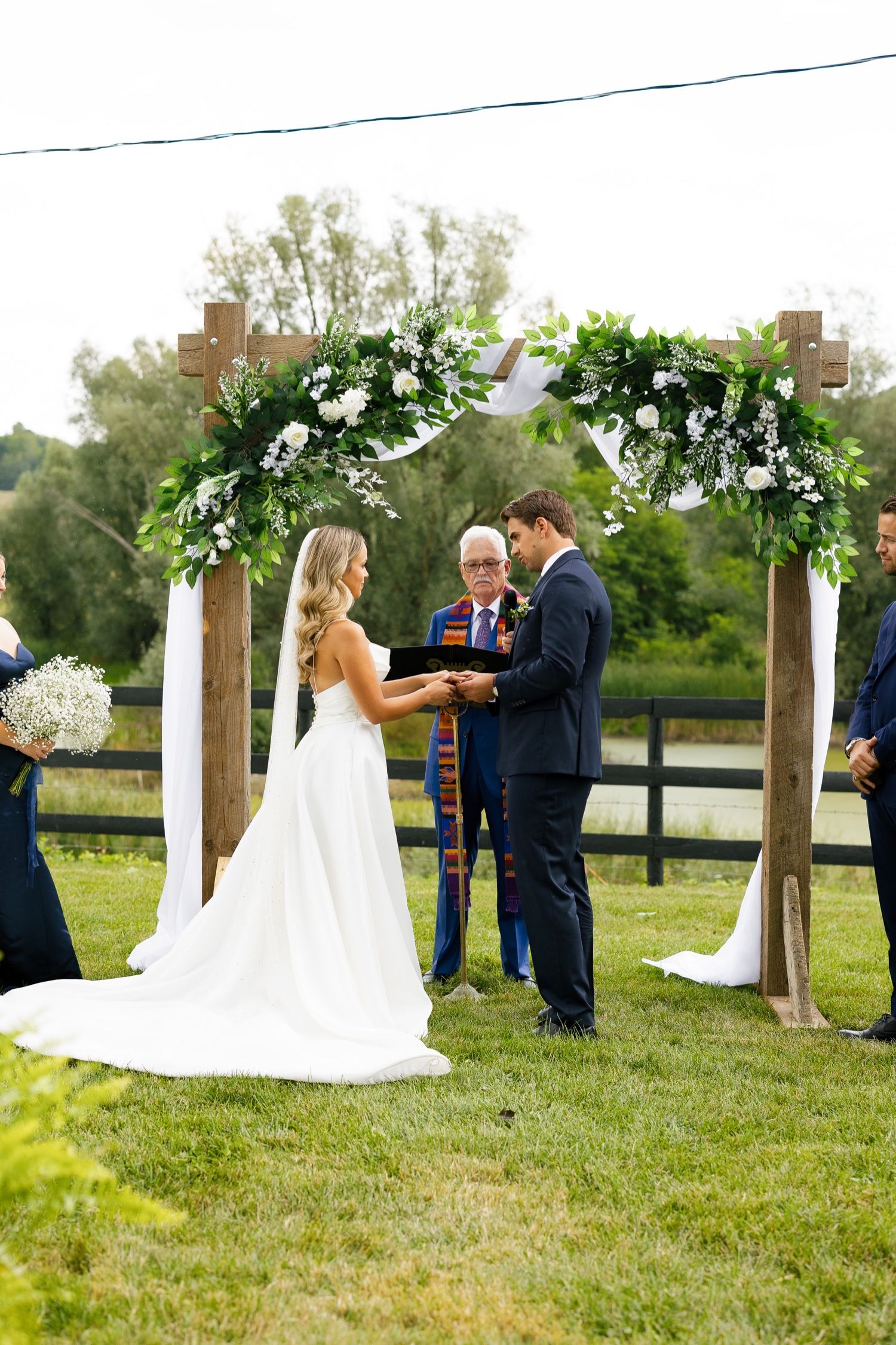 Intimate wedding ceremony moment under an arch decorated with white flowers and greenery.