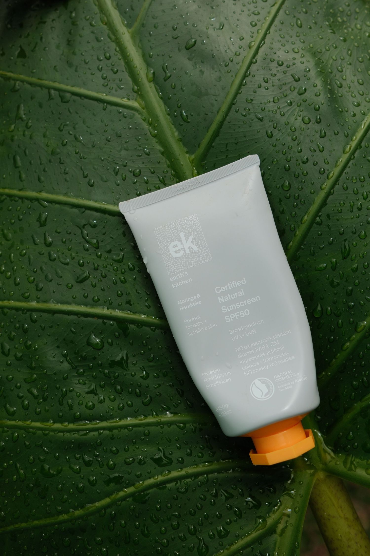 EK certified natural sunscreen SPF50 tube with orange cap on a wet tropical green leaf.