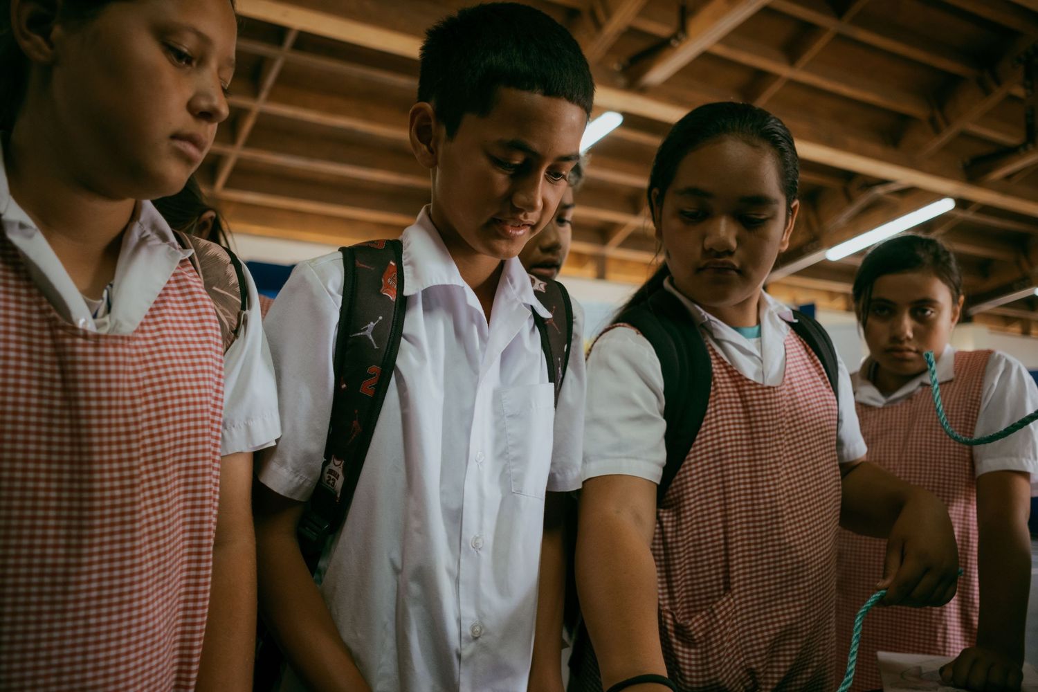 Students in school uniforms stand together with heads bowed in a wooden classroom setting.