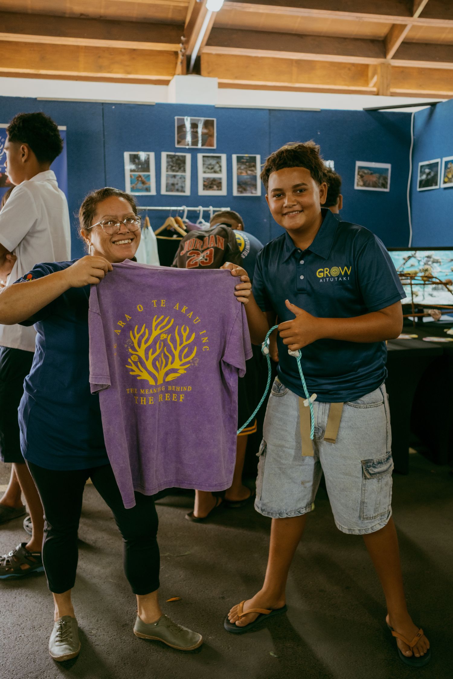 Two people proudly display a purple t-shirt with a coral design at a GROW Academy event.