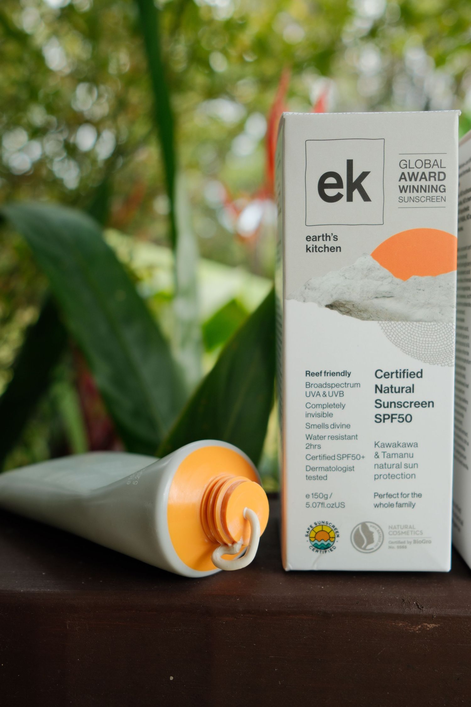 Earth's Kitchen EK Certified Natural SPF50 sunscreen tube and box displayed outdoors among tropical greenery.