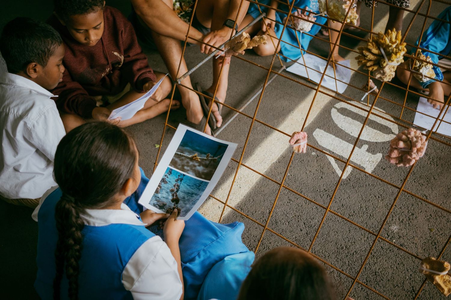 Children sit on tiled floor reviewing a photo book together in a classroom setting.