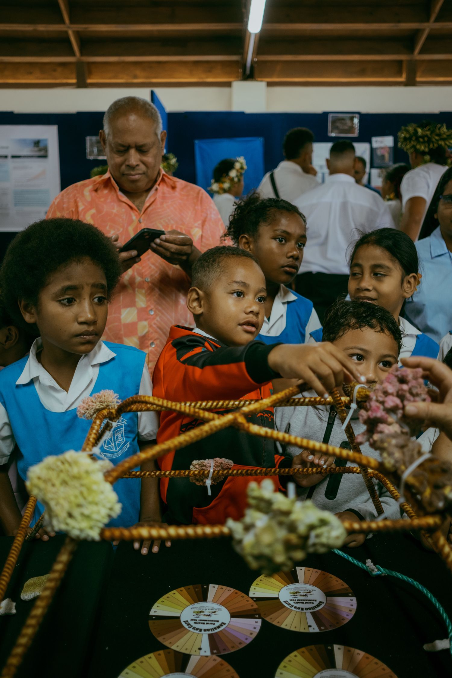 Children in school uniforms gather around a colorful display at an indoor cultural exhibition in Fiji.