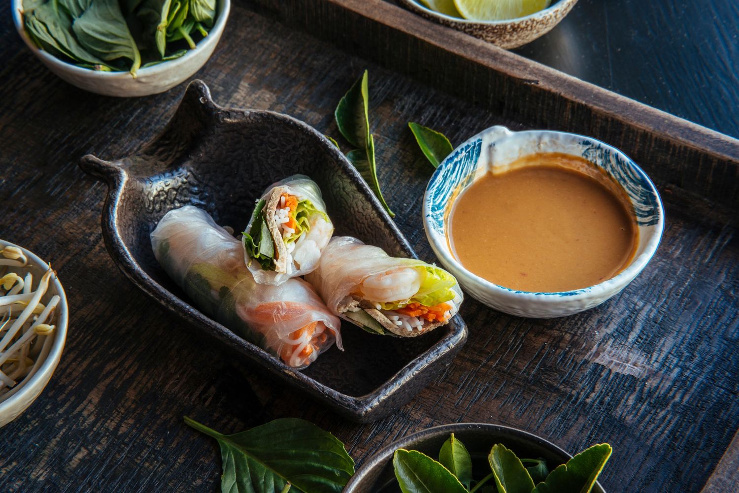 Fresh Vietnamese spring rolls with colorful vegetables served with a creamy peanut dipping sauce on a dark tray.
