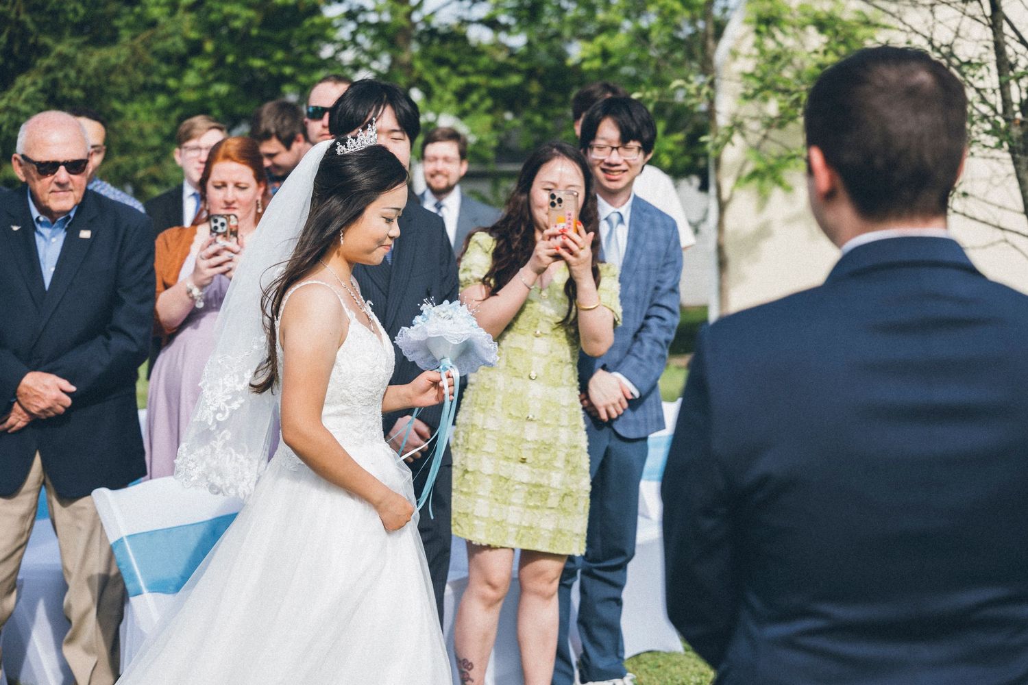 Emotional outdoor wedding ceremony with bride in white gown, guests smiling and crying with joy in sunny garden setting.
