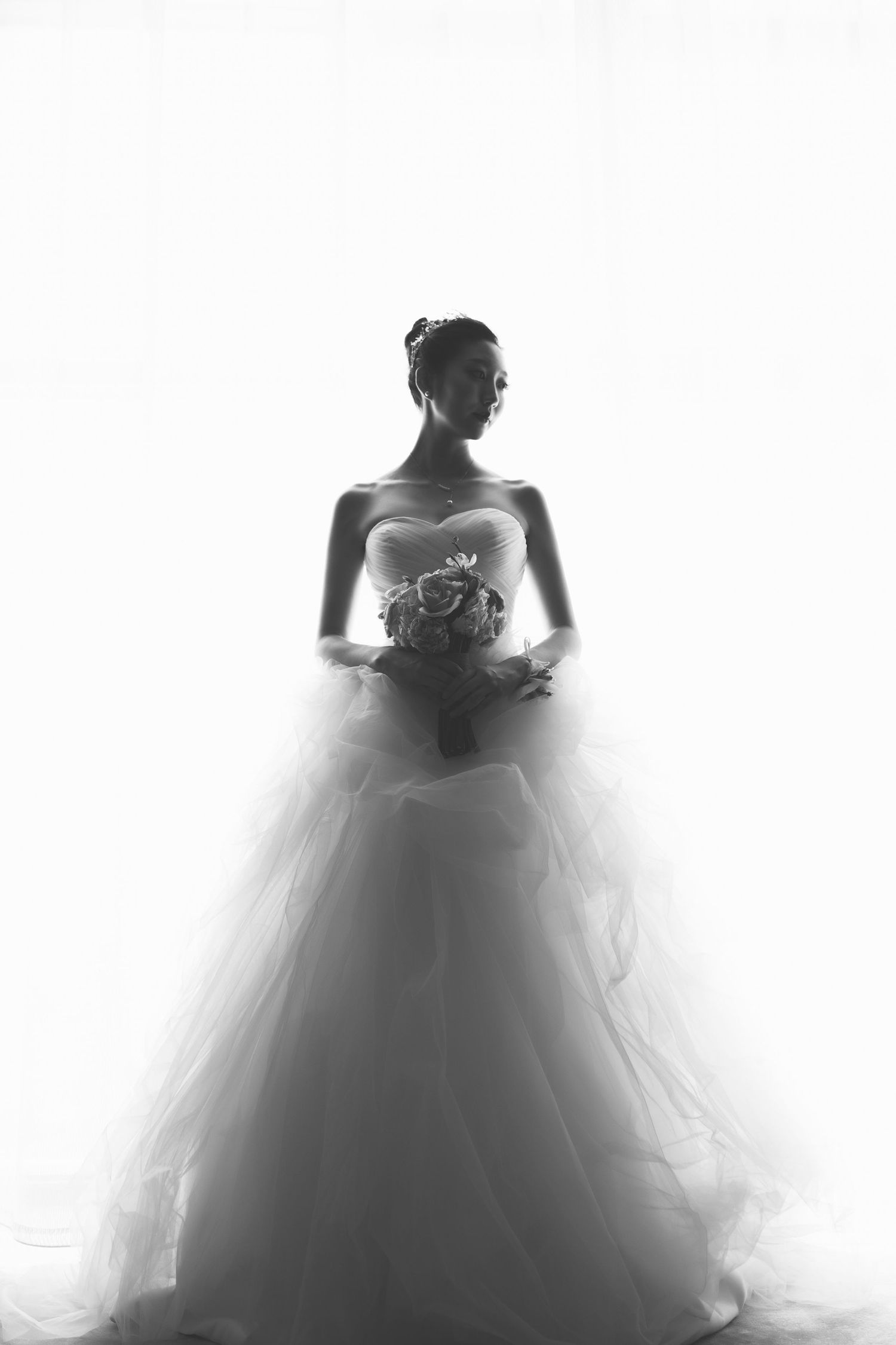Elegant bride in a strapless ball gown holds a bouquet in a dreamy black and white silhouette portrait.
