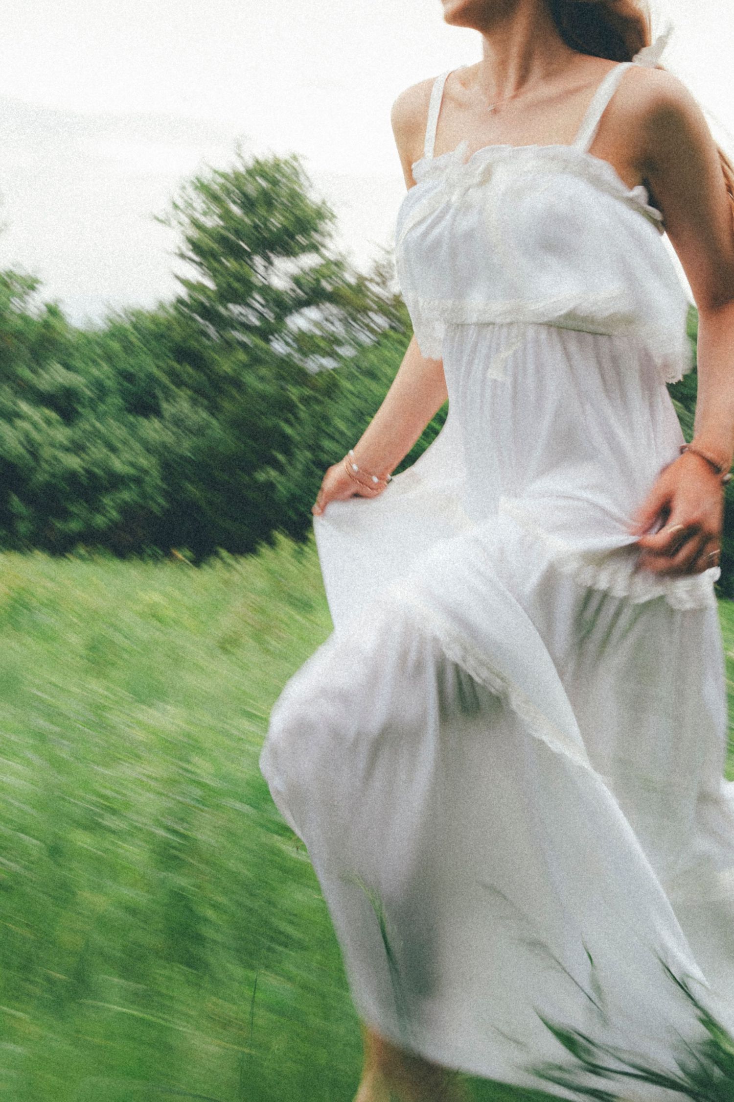 Woman in flowing white sundress running through lush green meadow, motion blur capturing carefree summer movement.