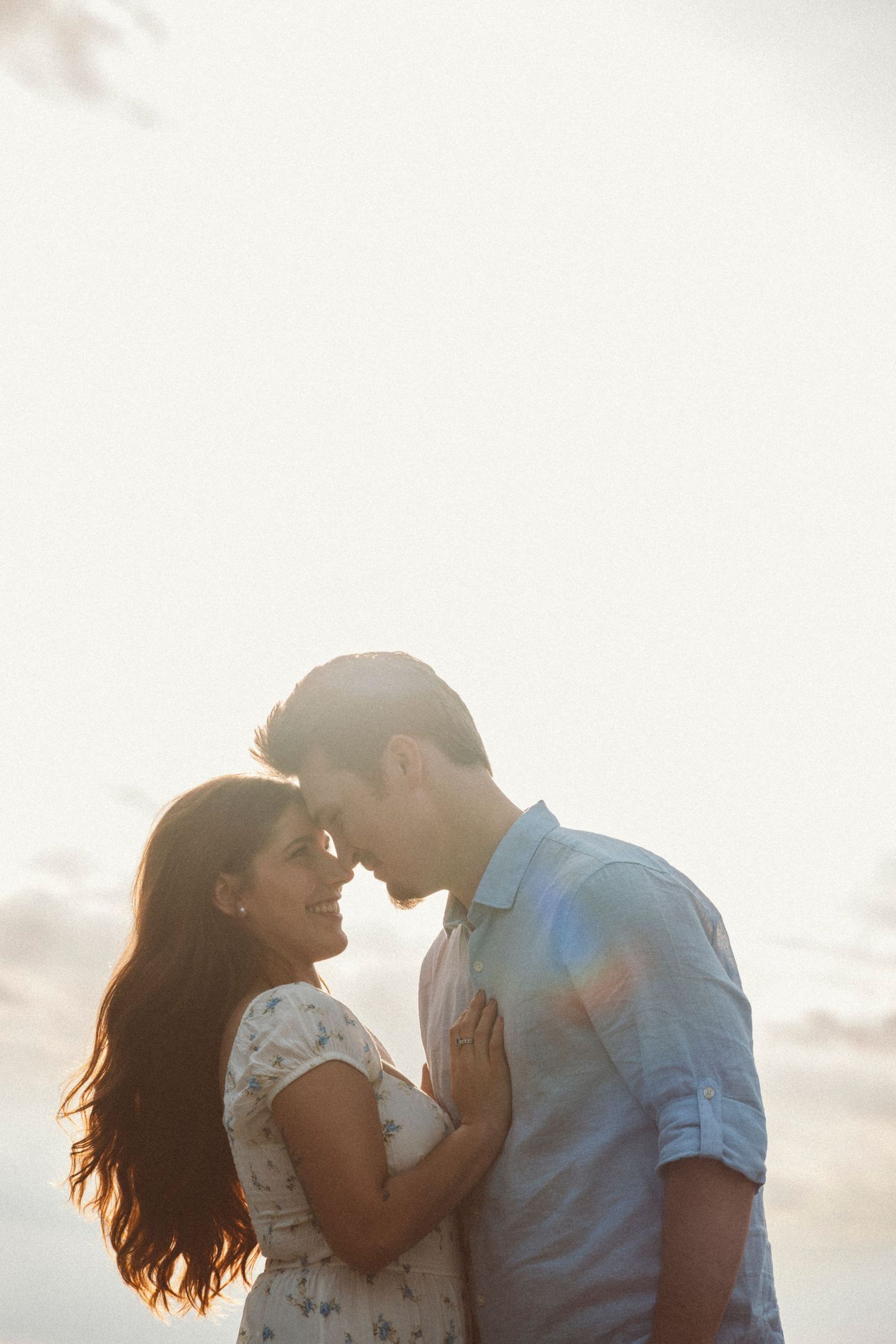Romantic couple touching foreheads in a tender moment with soft golden backlight at sunset.