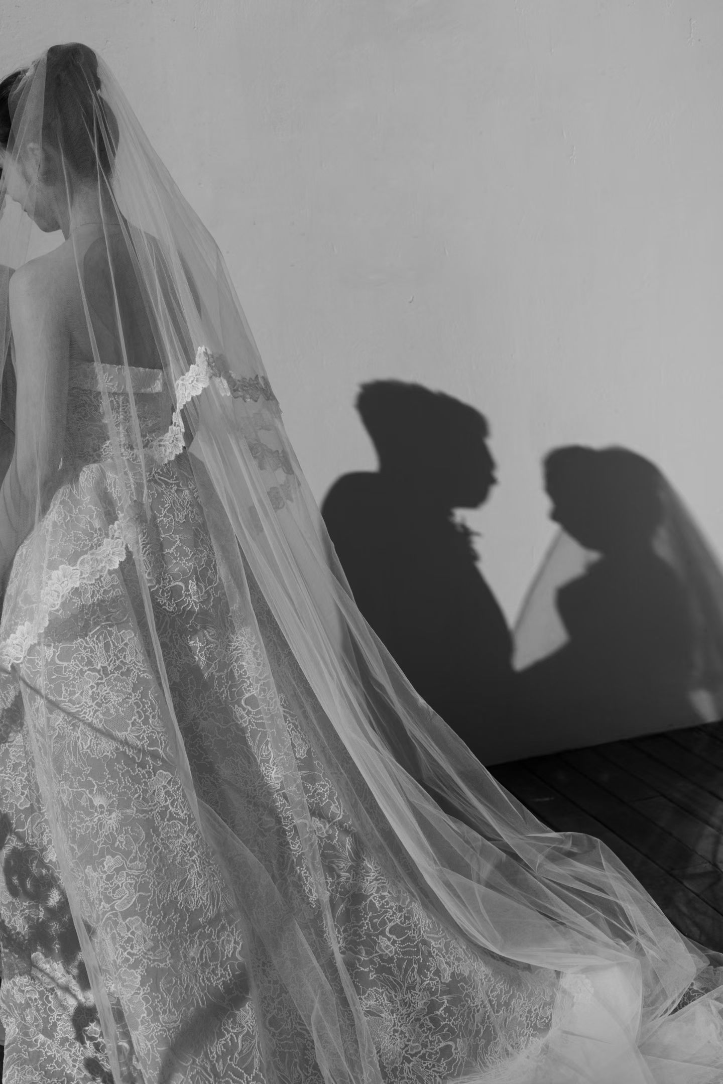 Black and white bridal portrait with elegant lace wedding dress and veil casting romantic shadows on wall.