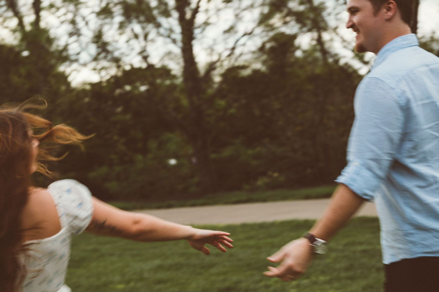 Smiling couple playing and reaching for each other in a green outdoor park.