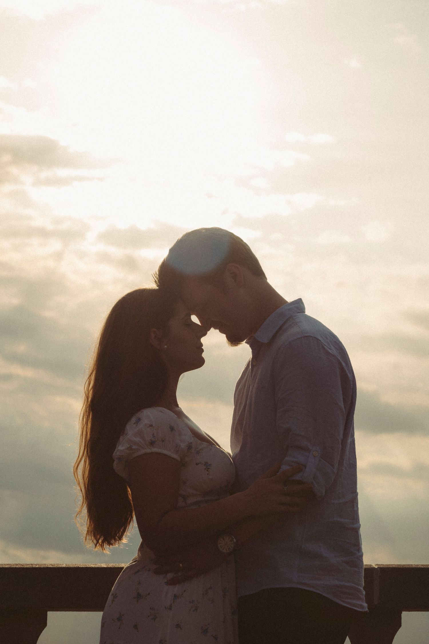 Romantic couple silhouetted against a dramatic sunset sky, leaning in close for a kiss outdoors.