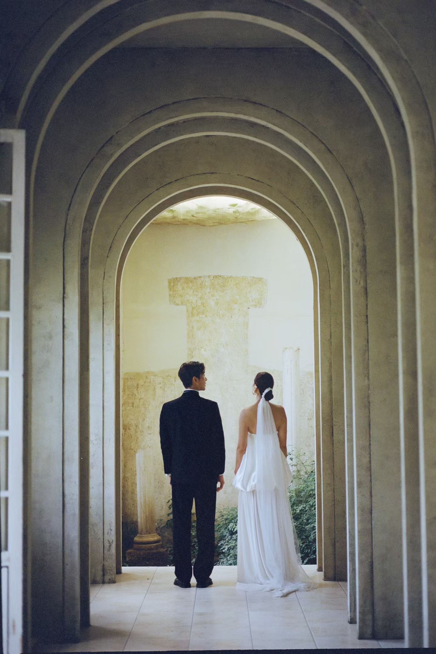 Bride and groom standing together beneath elegant stone arches in a beautiful classical venue.