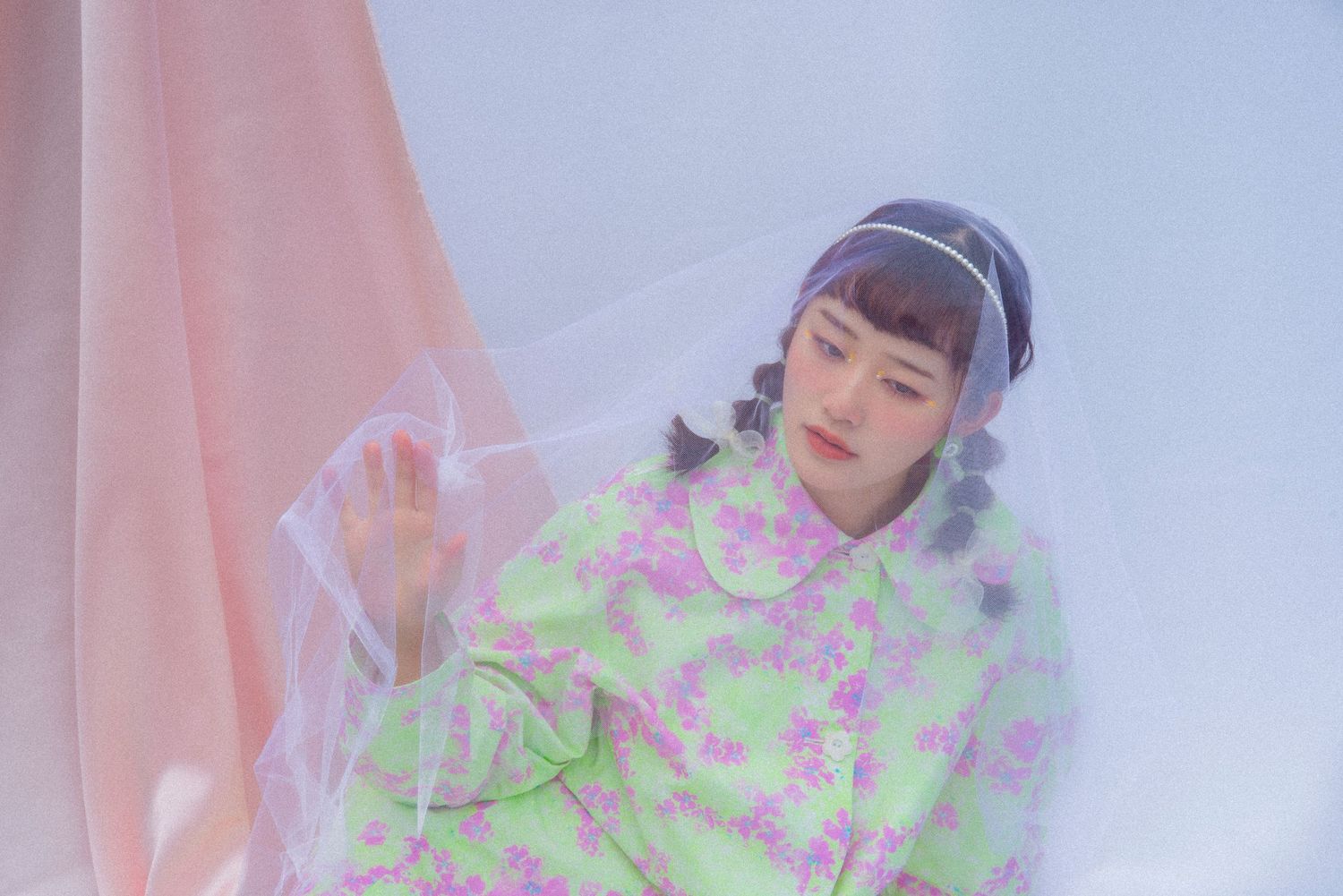 Young Asian woman in a green floral dress poses behind sheer pink fabric in a soft dreamy fashion editorial.