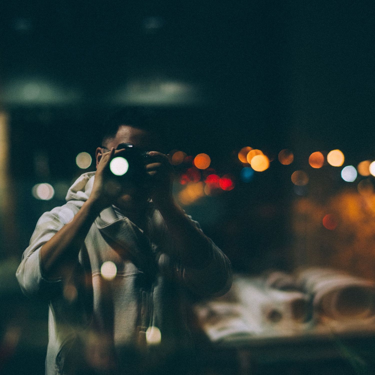 A photographer captures images at night with bokeh city lights glowing softly in the dark background.