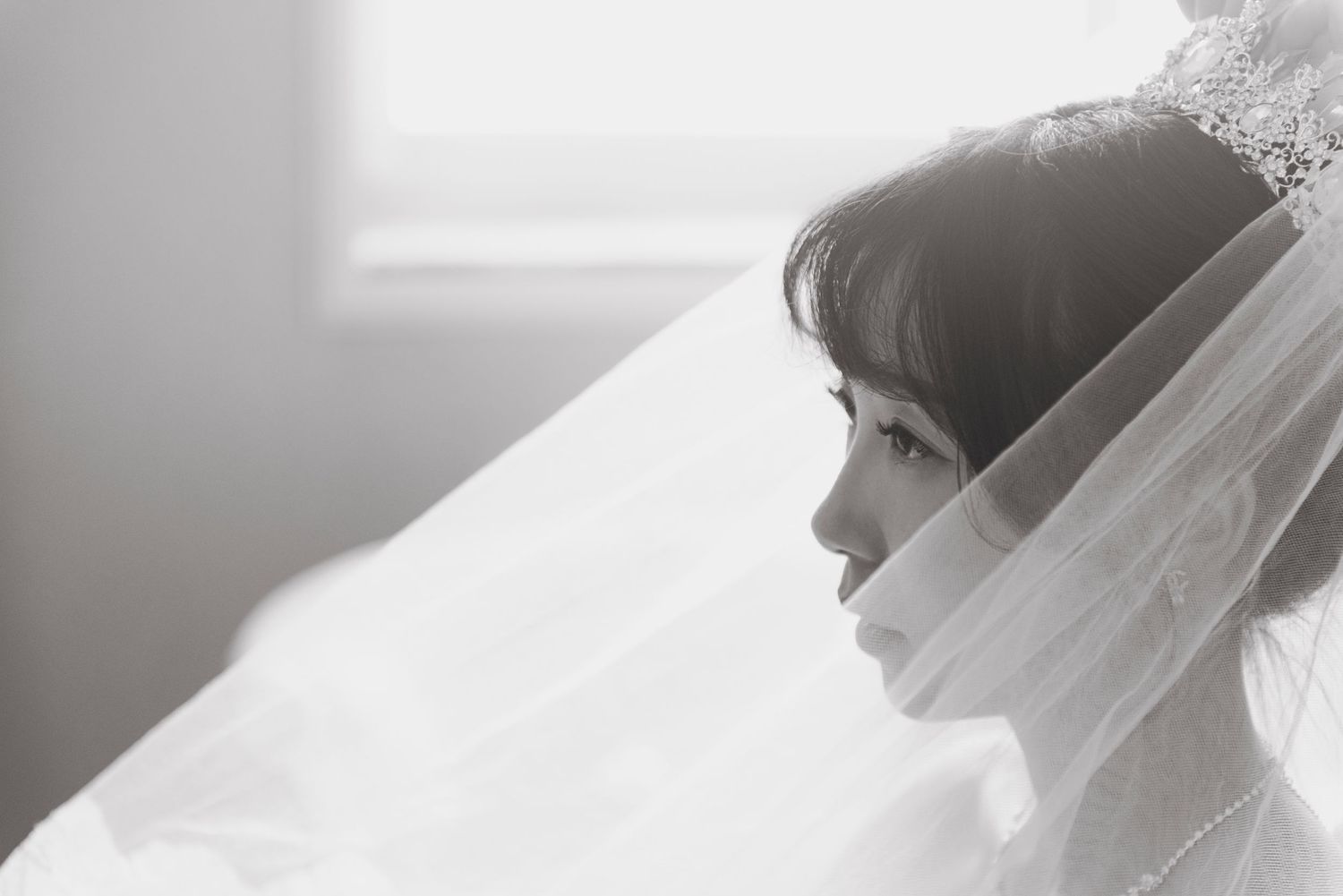 Elegant bride in white veil and tiara in a soft black and white portrait.