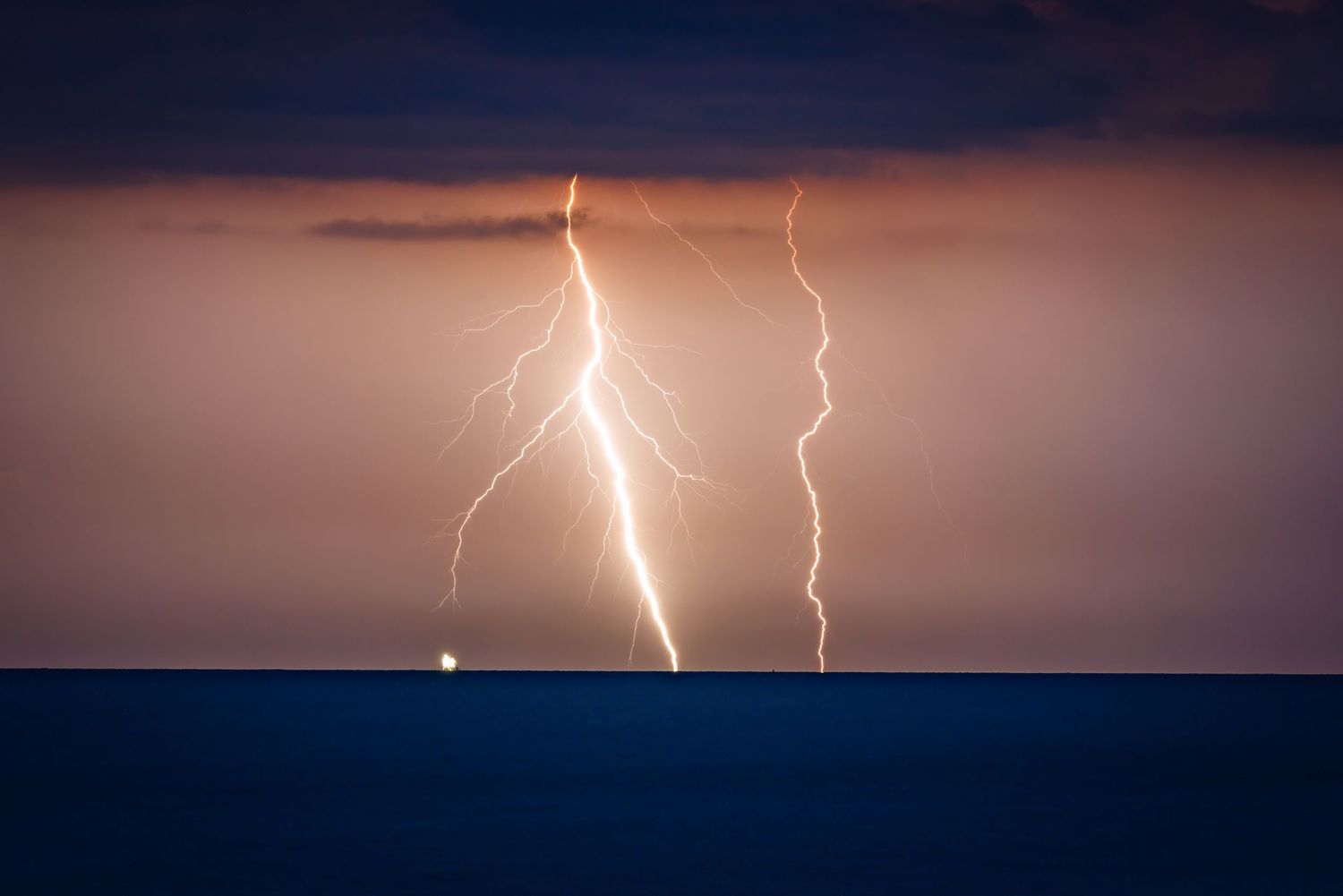 Two bright lightning bolts striking the ocean horizon against a dark stormy night sky.