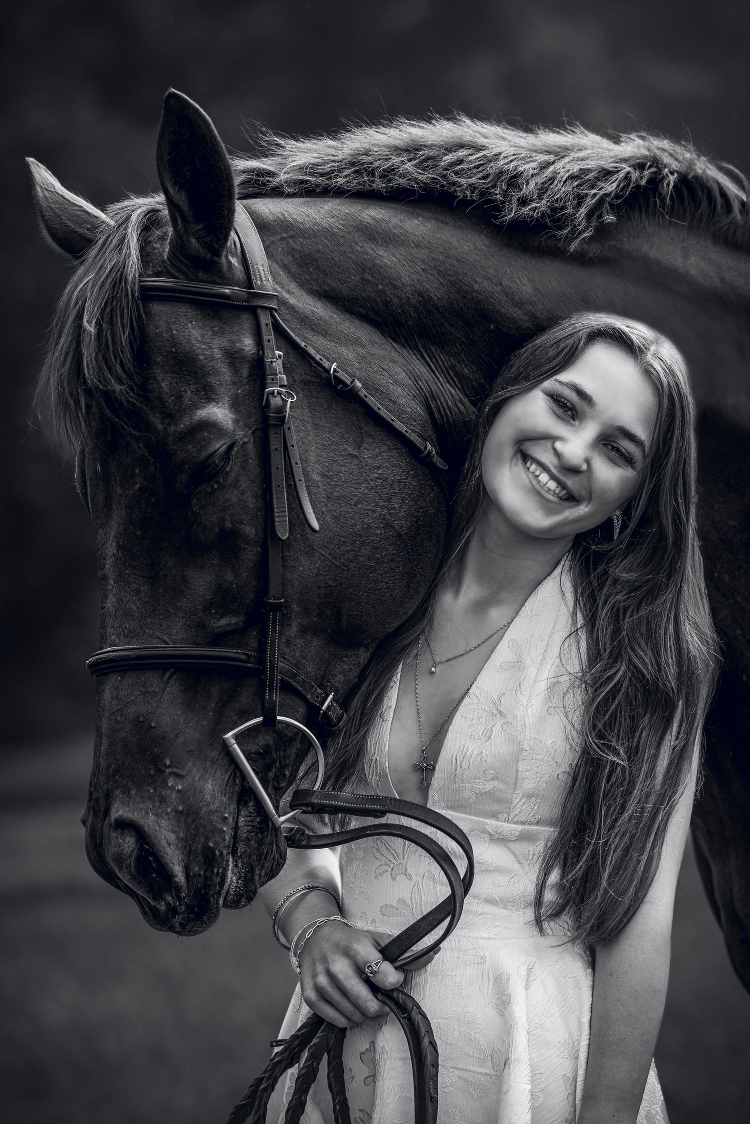 Black and white photo of a smiling young woman in a white dress holding reins beside a dark horse.