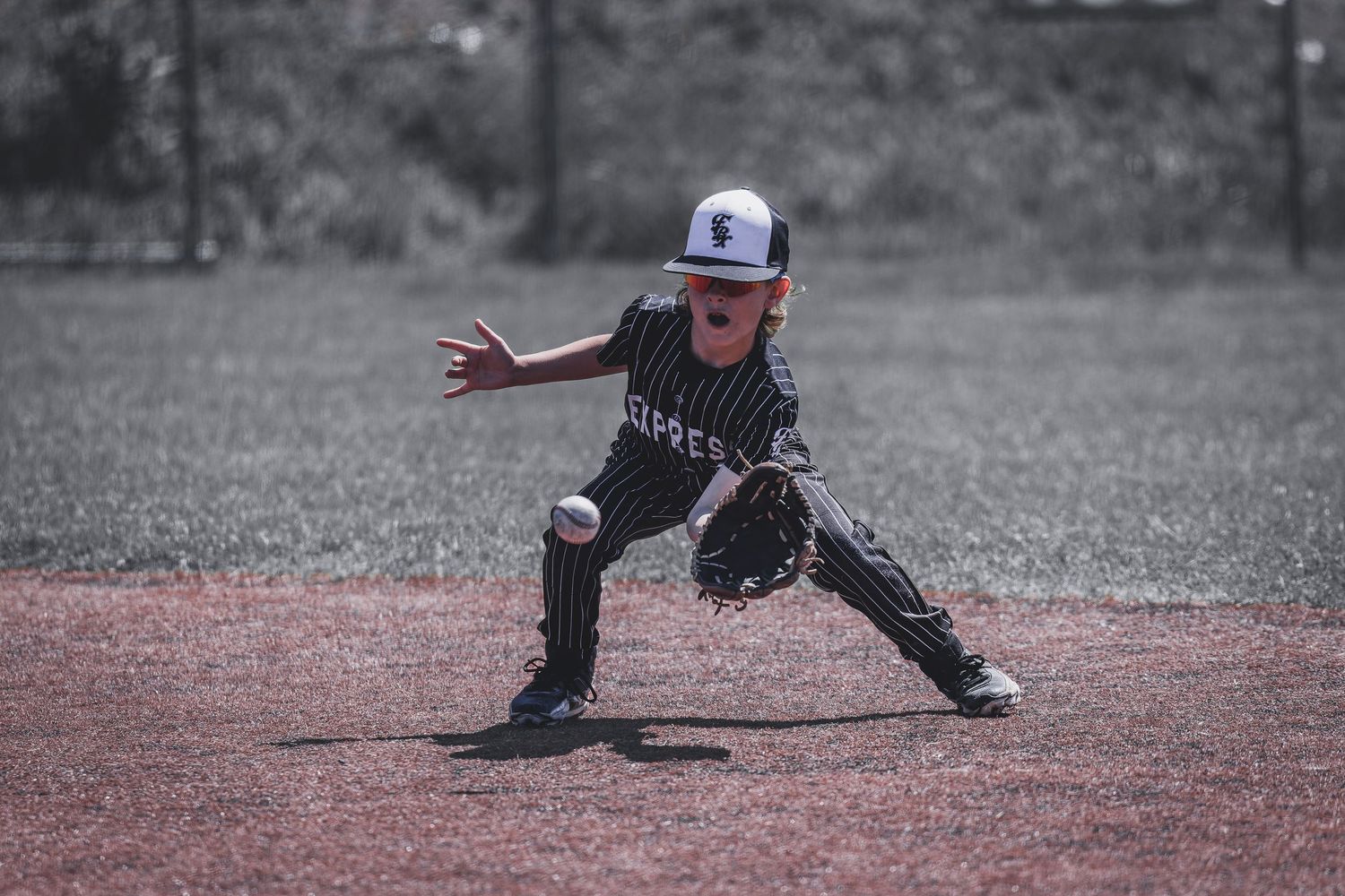 Young baseball player fielding a ground ball on the diamond in a black and white action photo.