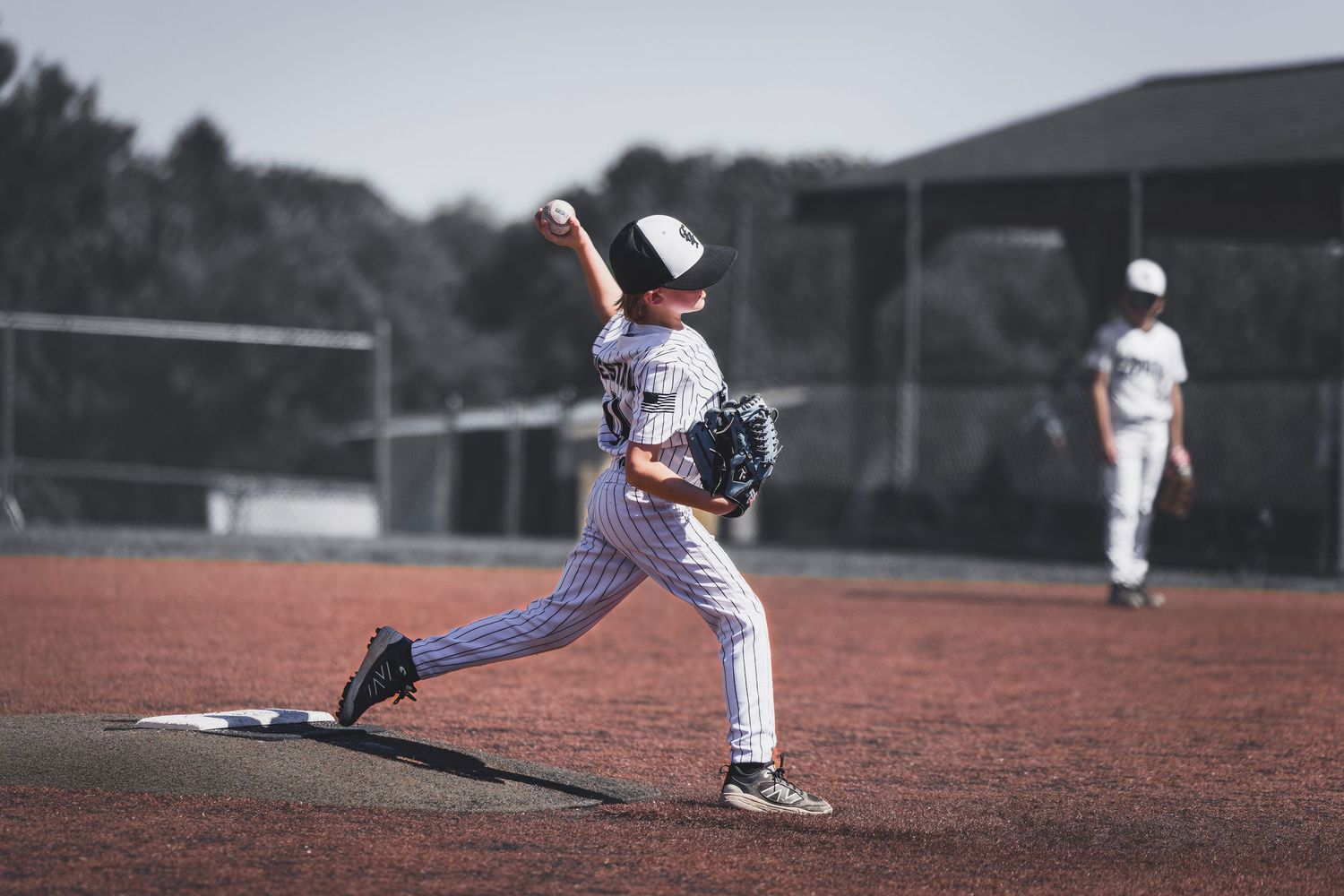Young baseball pitcher in white uniform delivers pitch on mound during youth game.