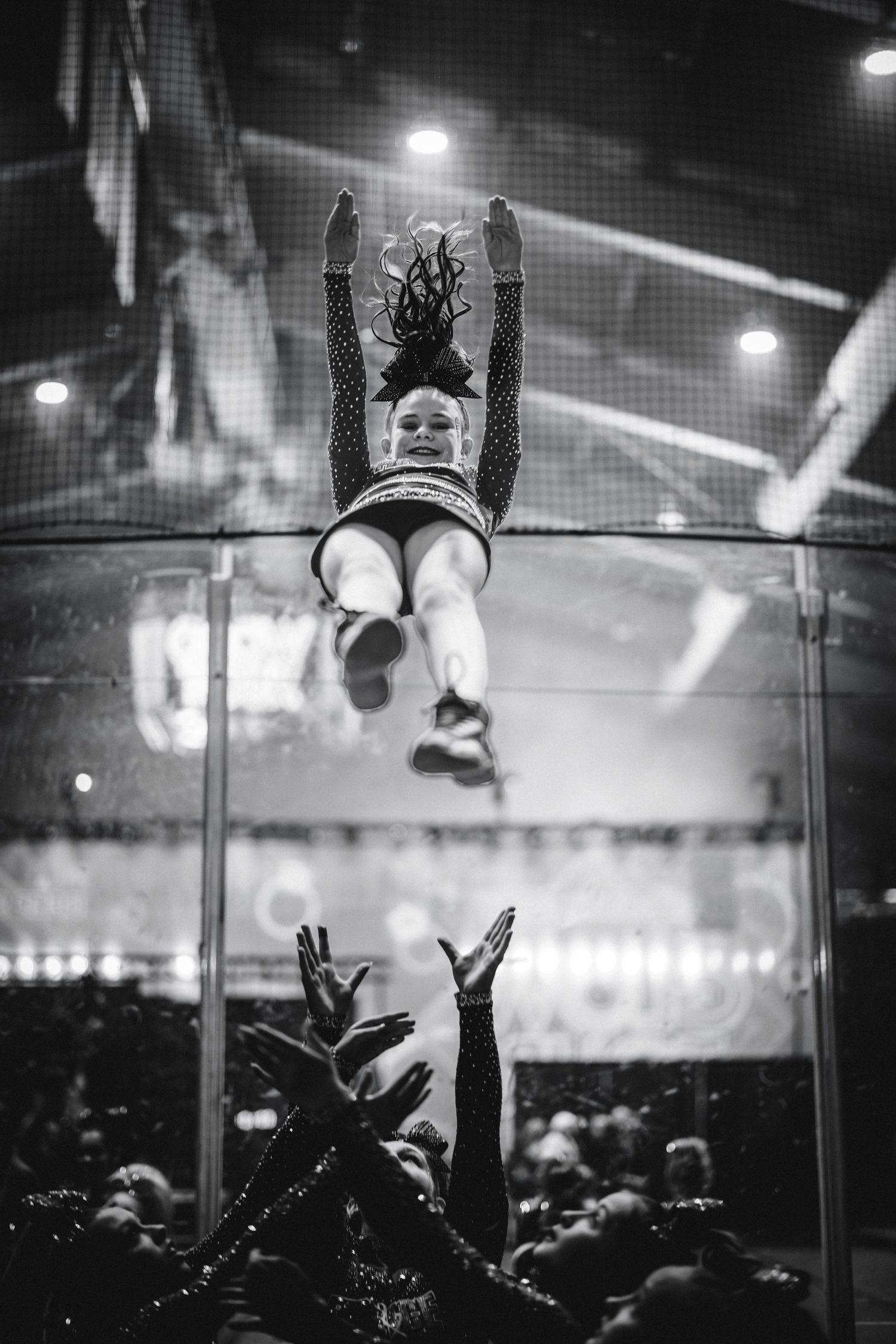 Black and white photo of cheerleader being tossed high in the air by teammates at competition.