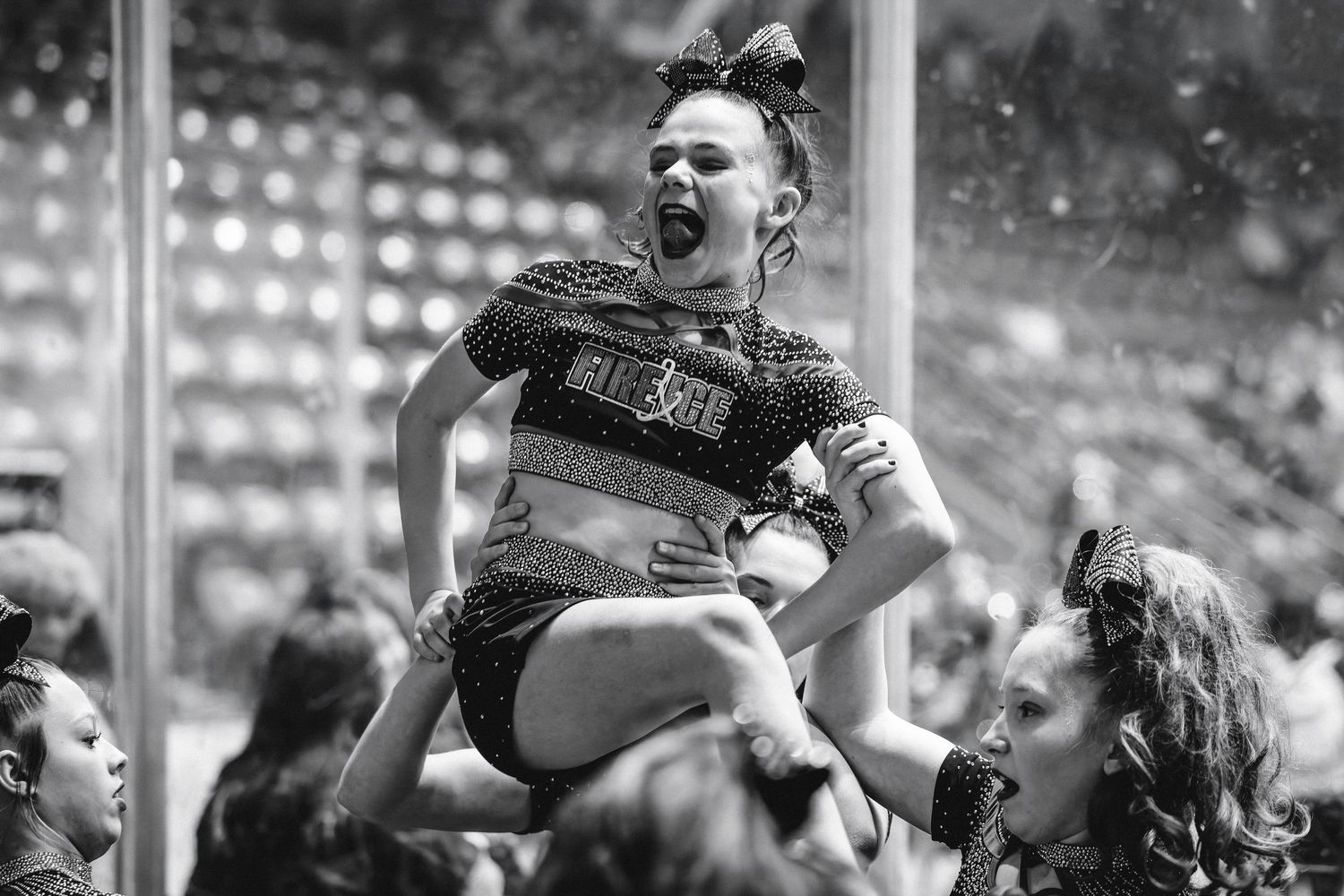 Black and white action shot of cheerleader being lifted high in the air during competitive cheerleading performance.