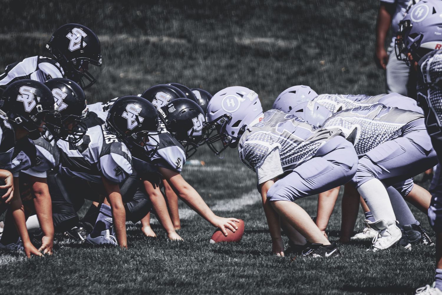 Youth football players lined up at scrimmage line ready for snap during an outdoor daytime game.