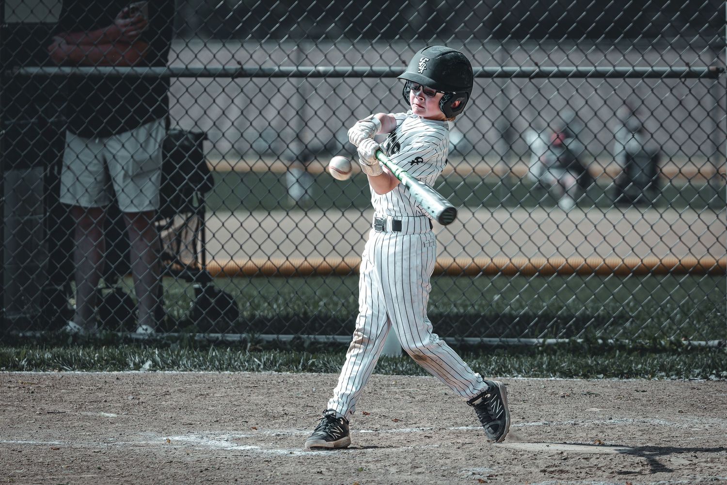 Young baseball player in green uniform swinging bat at home plate during little league game.