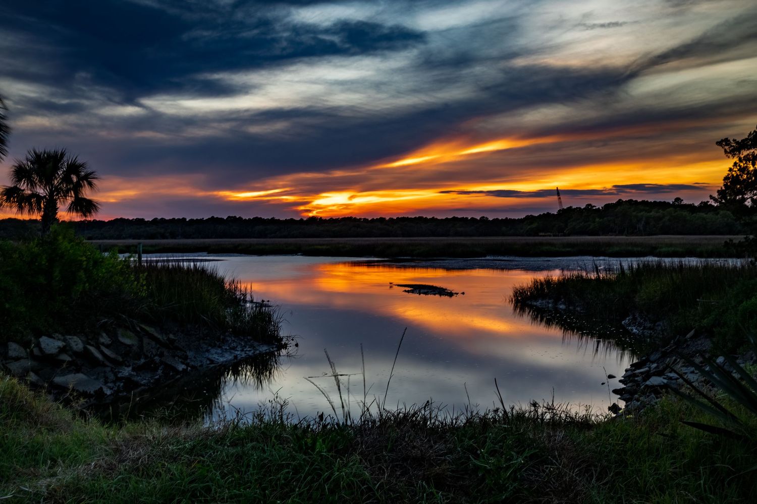 Vibrant orange and red sunset reflecting over a calm coastal wetland.