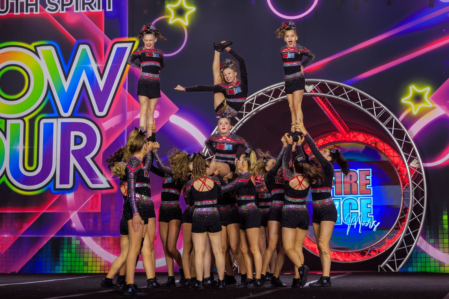 A youth cheerleading squad performs an impressive pyramid stunt at a competitive cheer tournament.