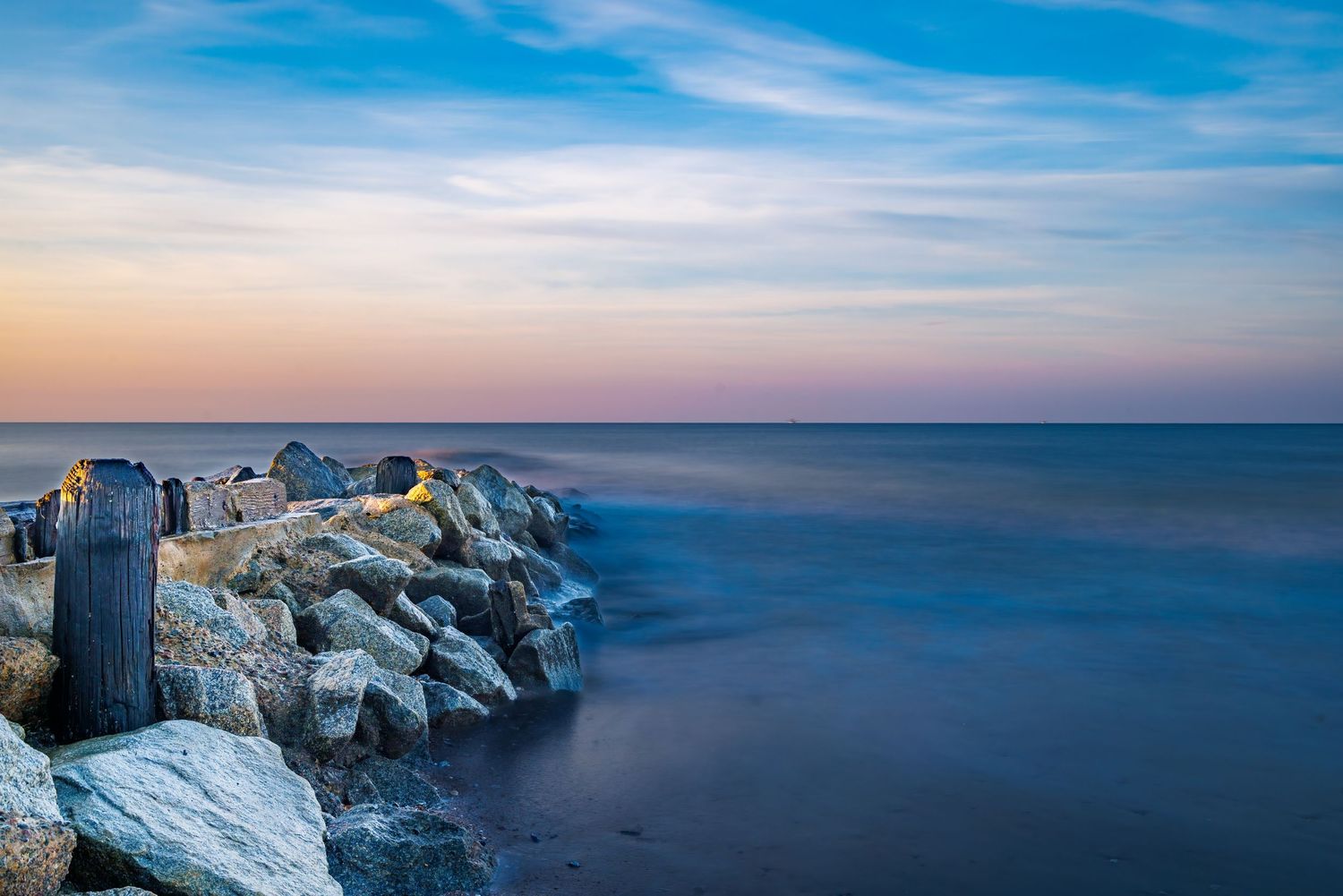 Rocky jetty extending into calm blue ocean waters at twilight with a pastel sky.