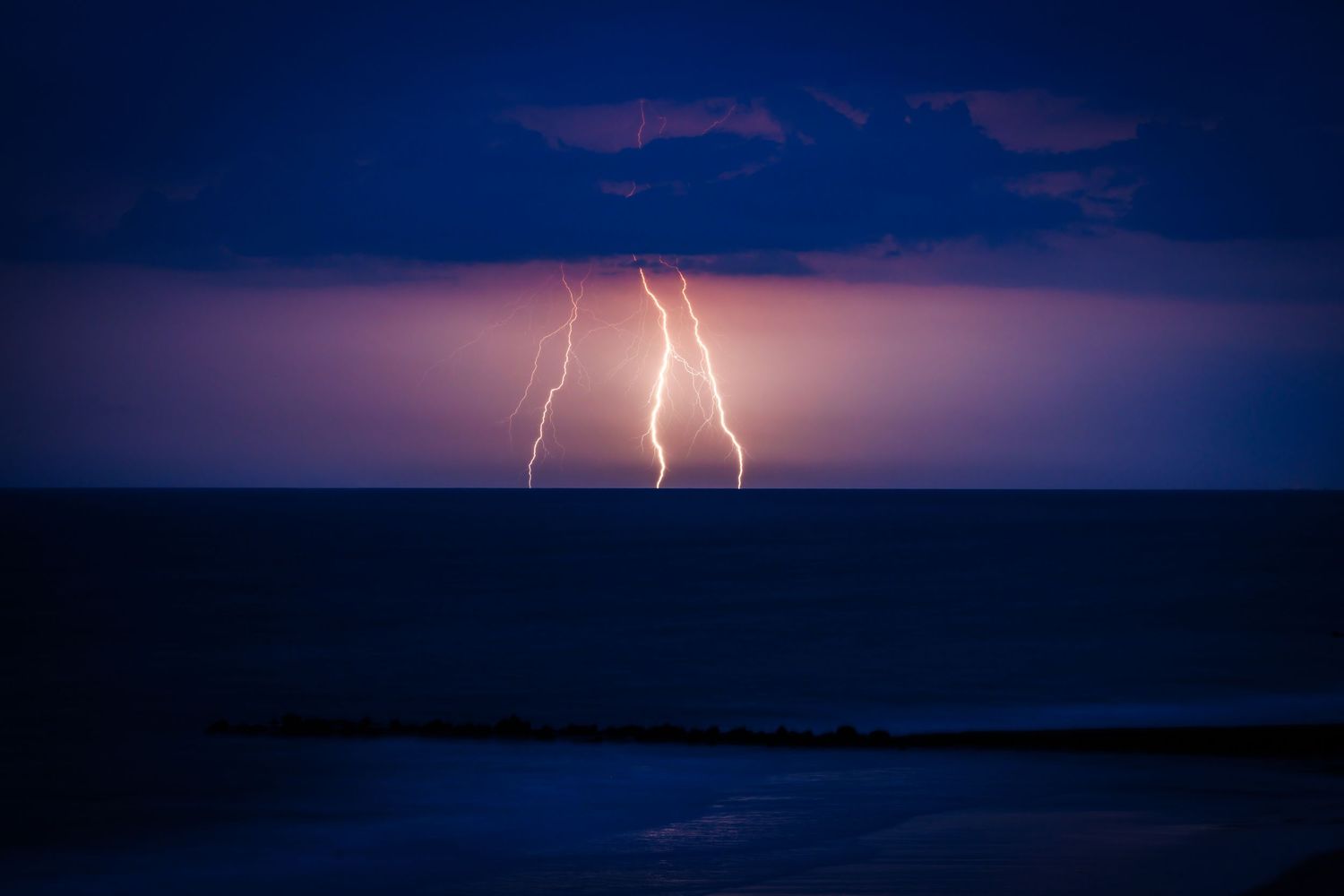 Double lightning strike over calm dark ocean waters during a nighttime coastal thunderstorm.
