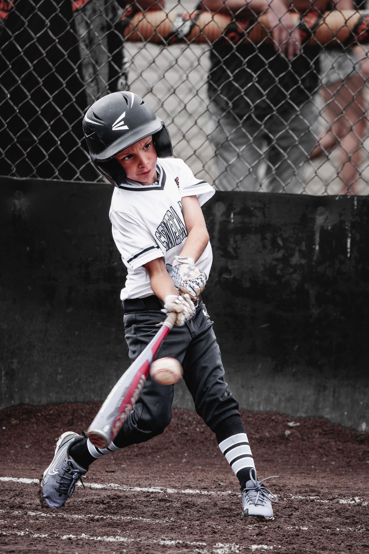 Young baseball batter in helmet making contact with pitch during youth baseball game at home plate.