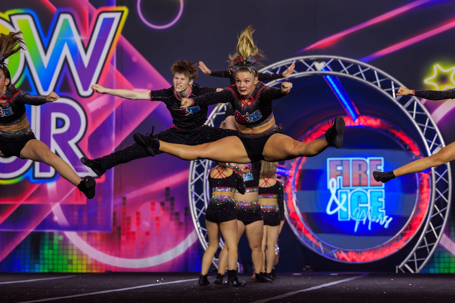 Cheerleaders performing aerial stunts at Fire and Ice Championship competition on colorful neon-lit stage.