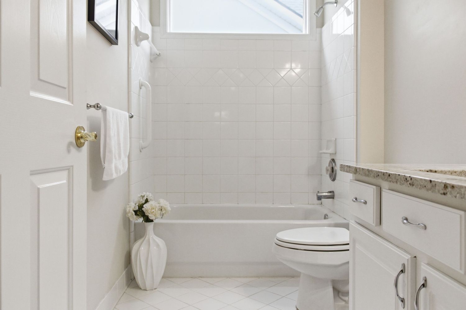 Clean white bathroom with subway tile shower, toilet, and granite vanity with modern fixtures.
