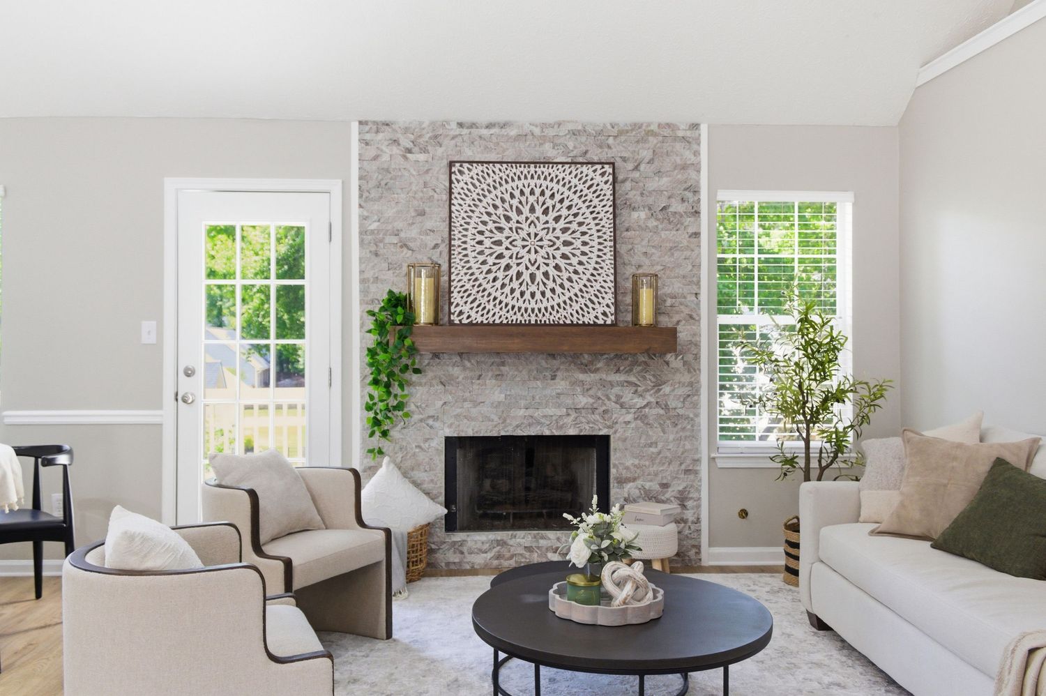 Bright living room with stone fireplace, neutral furniture, arched decor, and large windows with greenery.