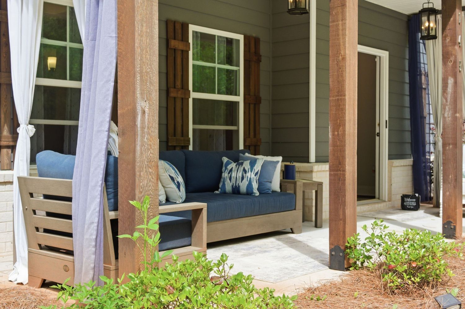 Cozy covered porch featuring a wooden daybed swing with navy cushions and patterned throw pillows.