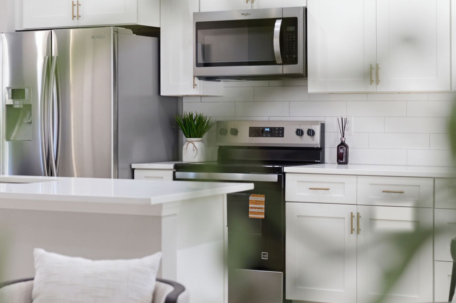 Modern white kitchen with stainless steel appliances, subway tile backsplash, and gold cabinet hardware.