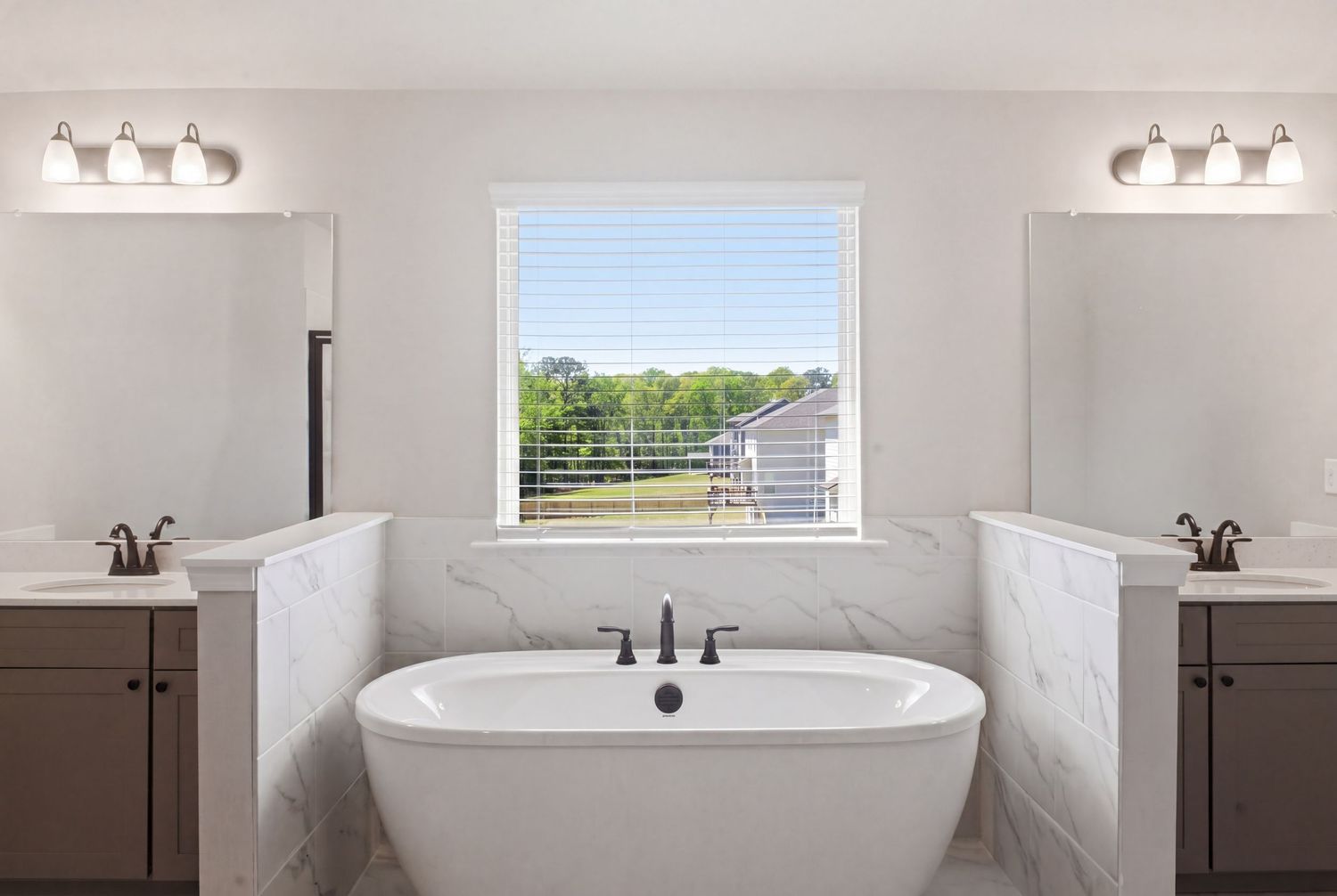 Elegant master bathroom with freestanding soaking tub, marble surround, dual vanities, and a bright window view.