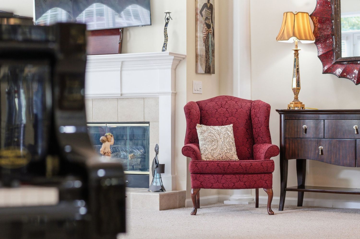 Classic living room with red wingback chair, white fireplace, and warm traditional decor.
