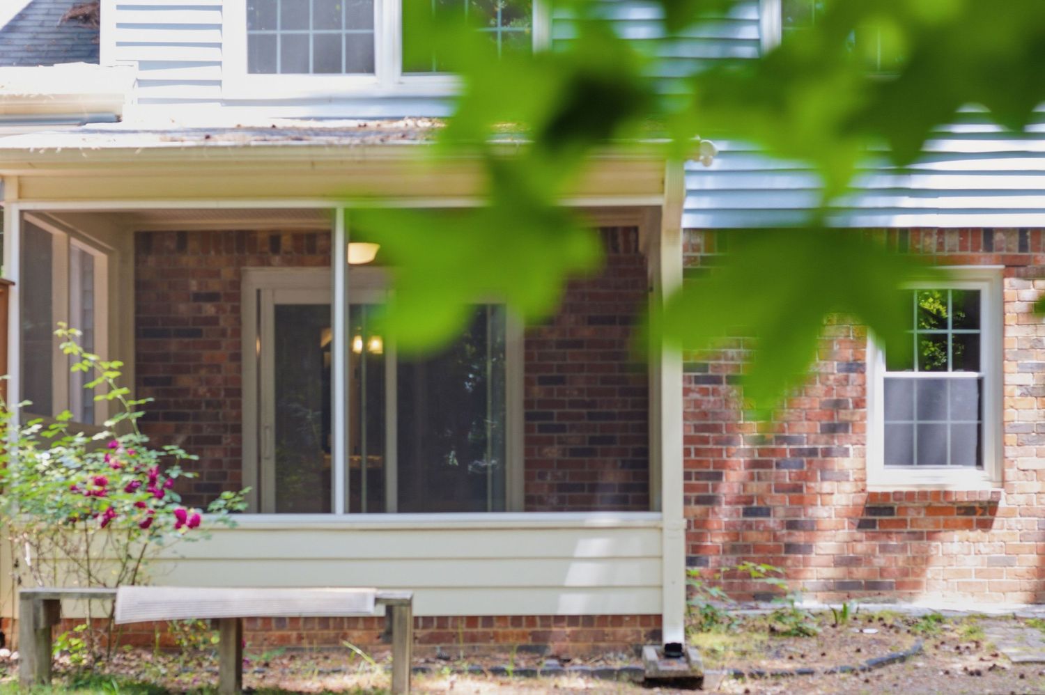 Brick home exterior with covered porch, sliding glass door, and lush green foliage in the foreground.