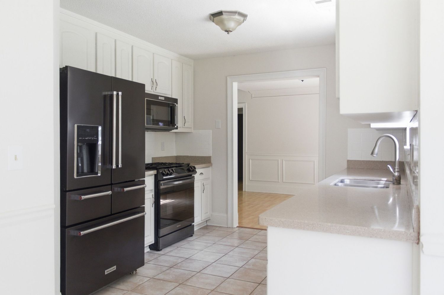 Clean white kitchen with black refrigerator, stainless steel appliances, tile flooring, and ample cabinet storage.