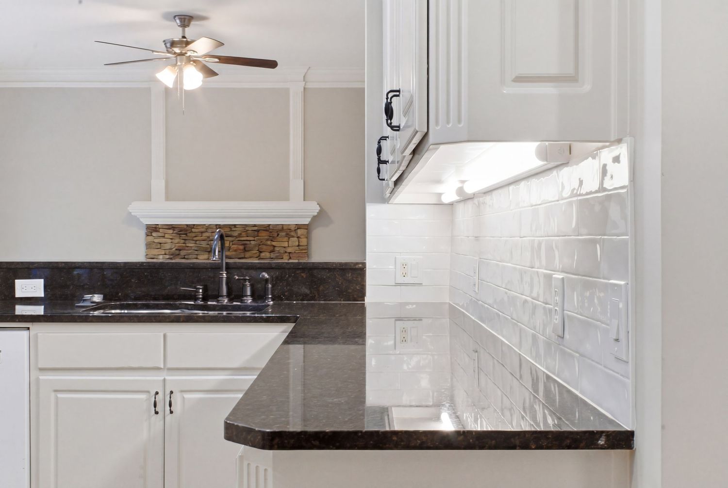 Modern kitchen with white cabinets, dark granite countertops, white subway tile backsplash, and ceiling fan.